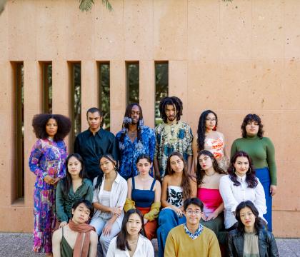 Group of fellows in front of a clay-colored wall, dressed in a natural palette of yellows, oranges, greens, and purples