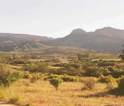 Landscape photo of rolling hills in a valley, with rocky outcroppings in the background and dry grass and trees in the foreground.