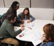 3 students sitting at a table with a tutor working with two students.